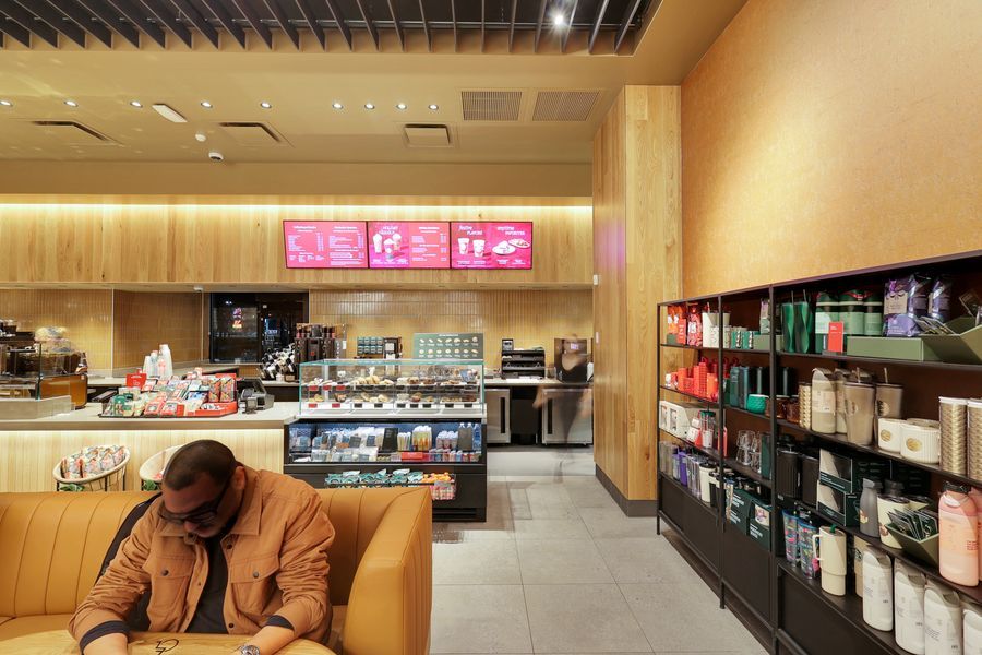 Modern Starbucks interior with wooden shelving, product displays, and a customer seated at a booth near the counter.