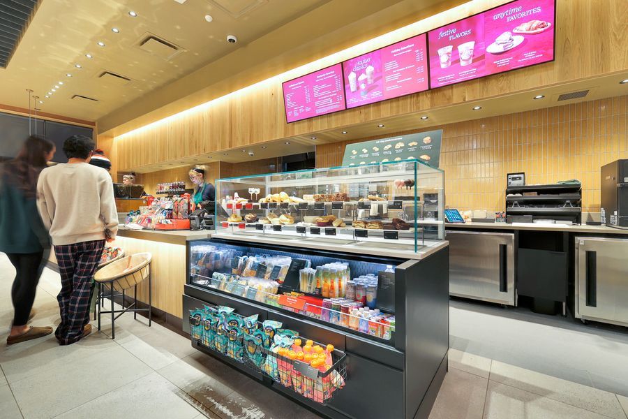 Modern Starbucks cafe interior with illuminated menu boards, display case with snacks, and customers ordering at the counter.