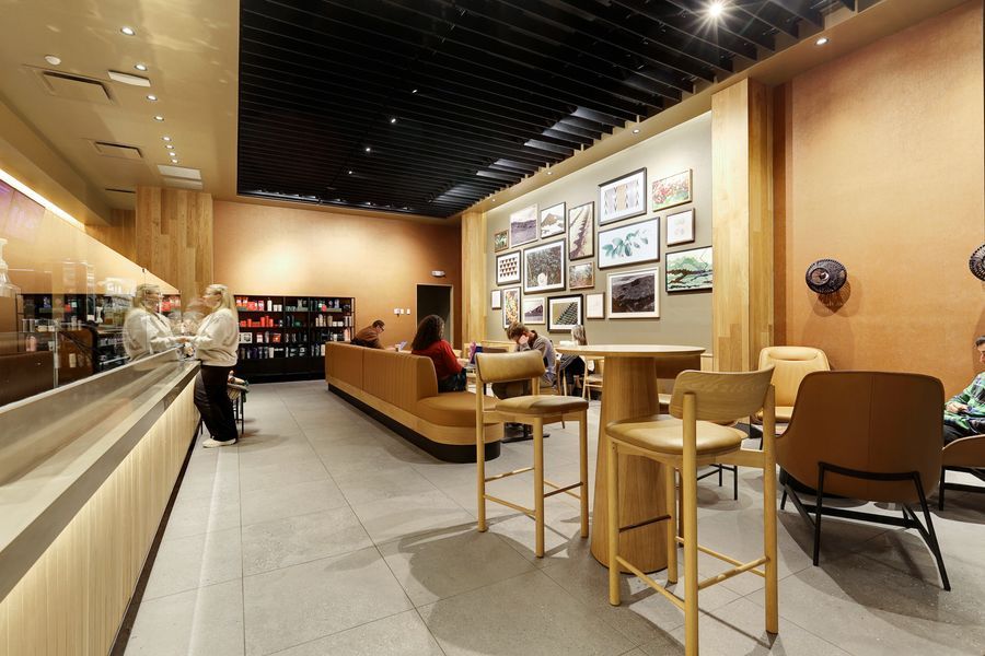 Modern Starbucks cafe interior featuring wooden bar seating, framed artwork gallery wall, and warm ambient lighting.