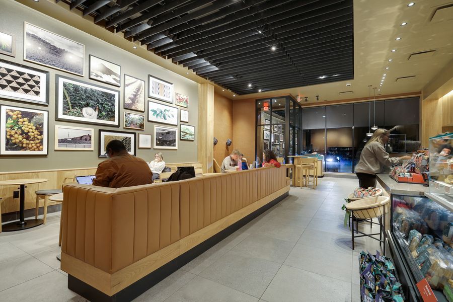 Modern Starbucks interior with warm wood paneling, framed artwork gallery wall, and customers seated at a long counter.