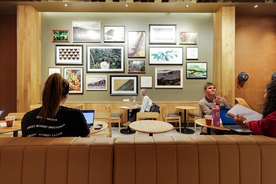 Customers relaxing in a cozy Starbucks seating area with booth seats, wooden tables, and framed photos on the wall.