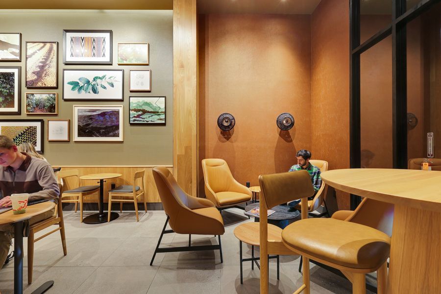 Cozy Starbucks seating area featuring tan leather chairs, wooden tables, and colorful framed artwork on cream walls.