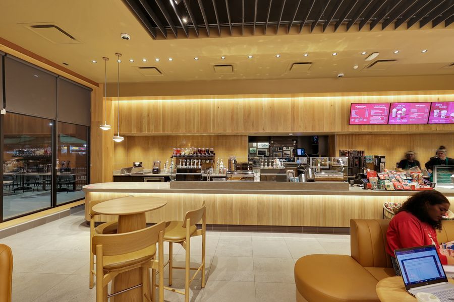 Bright cafe interior featuring wooden bar seating, pink digital menu boards, and a sleek service counter.