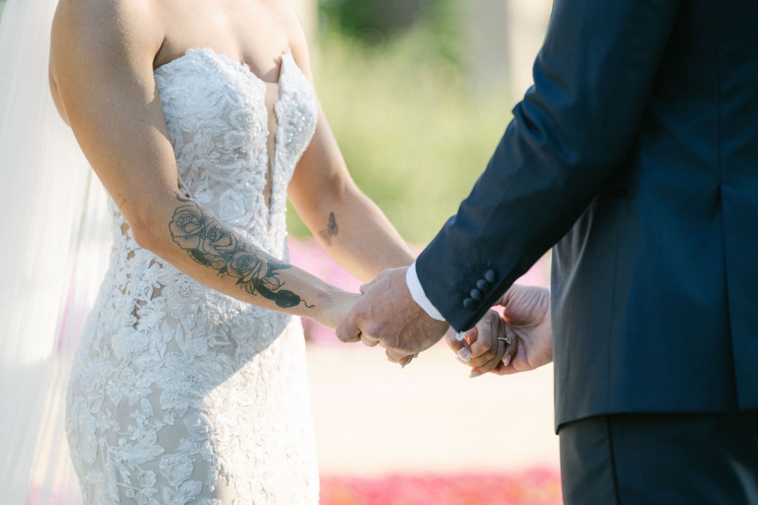Armour House Wedding - Bride and groom holding hands during wedding ceremony, bride wearing lace gown with floral tattoo.