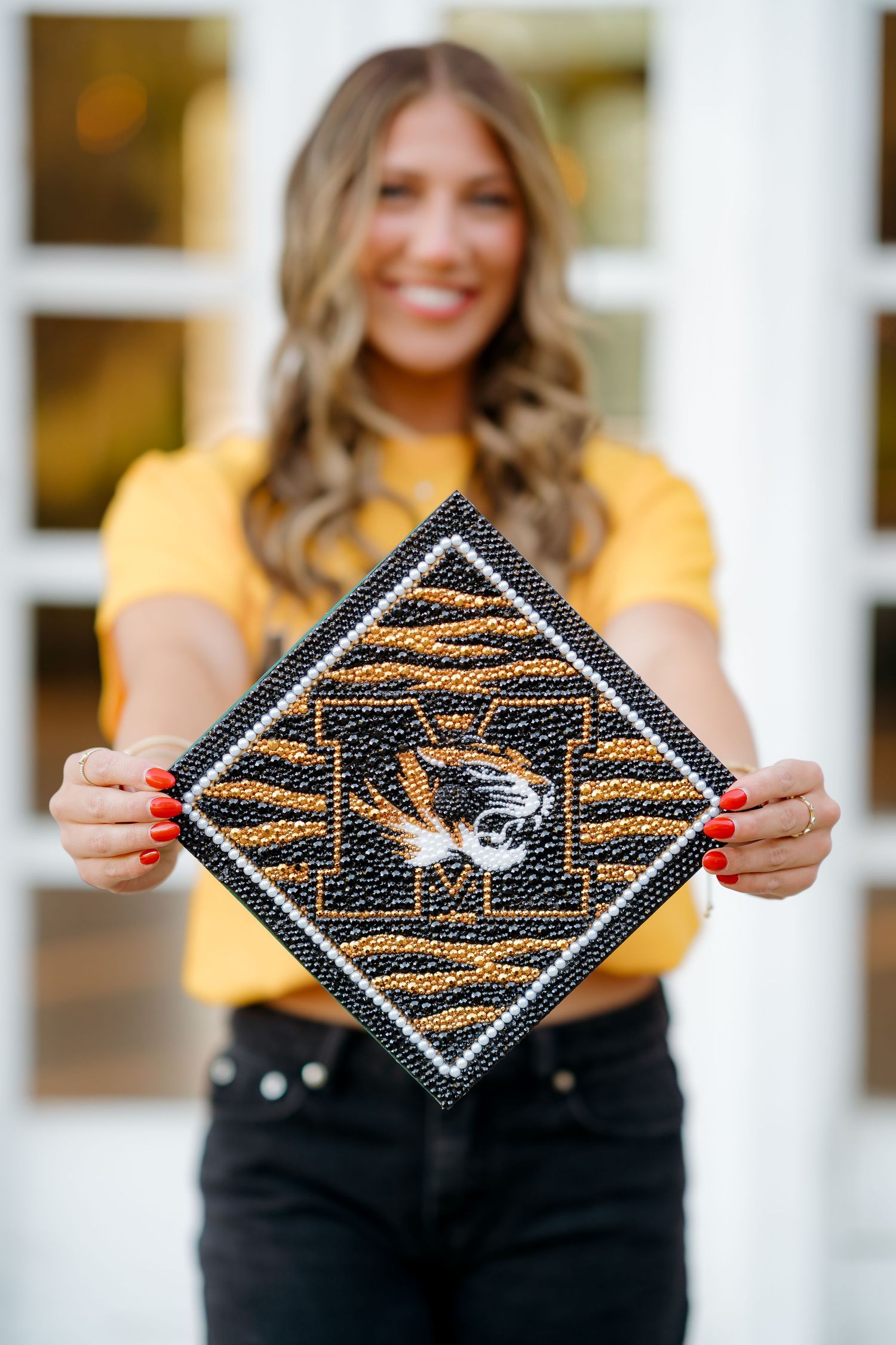 Smiling graduate holds decorated University of Missouri tiger-print graduation cap with black and gold beaded design.