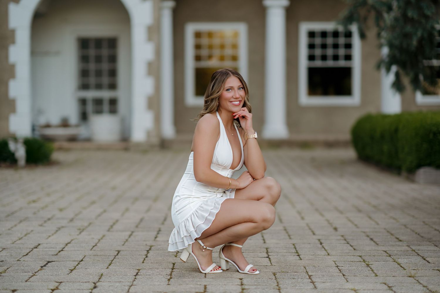 Woman in white mini dress posing outdoors in front of a stone building.