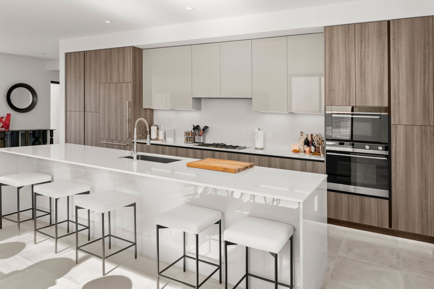 Modern kitchen with white quartz island, bar stools, wood-tone cabinetry, stainless steel appliances, and marble flooring.