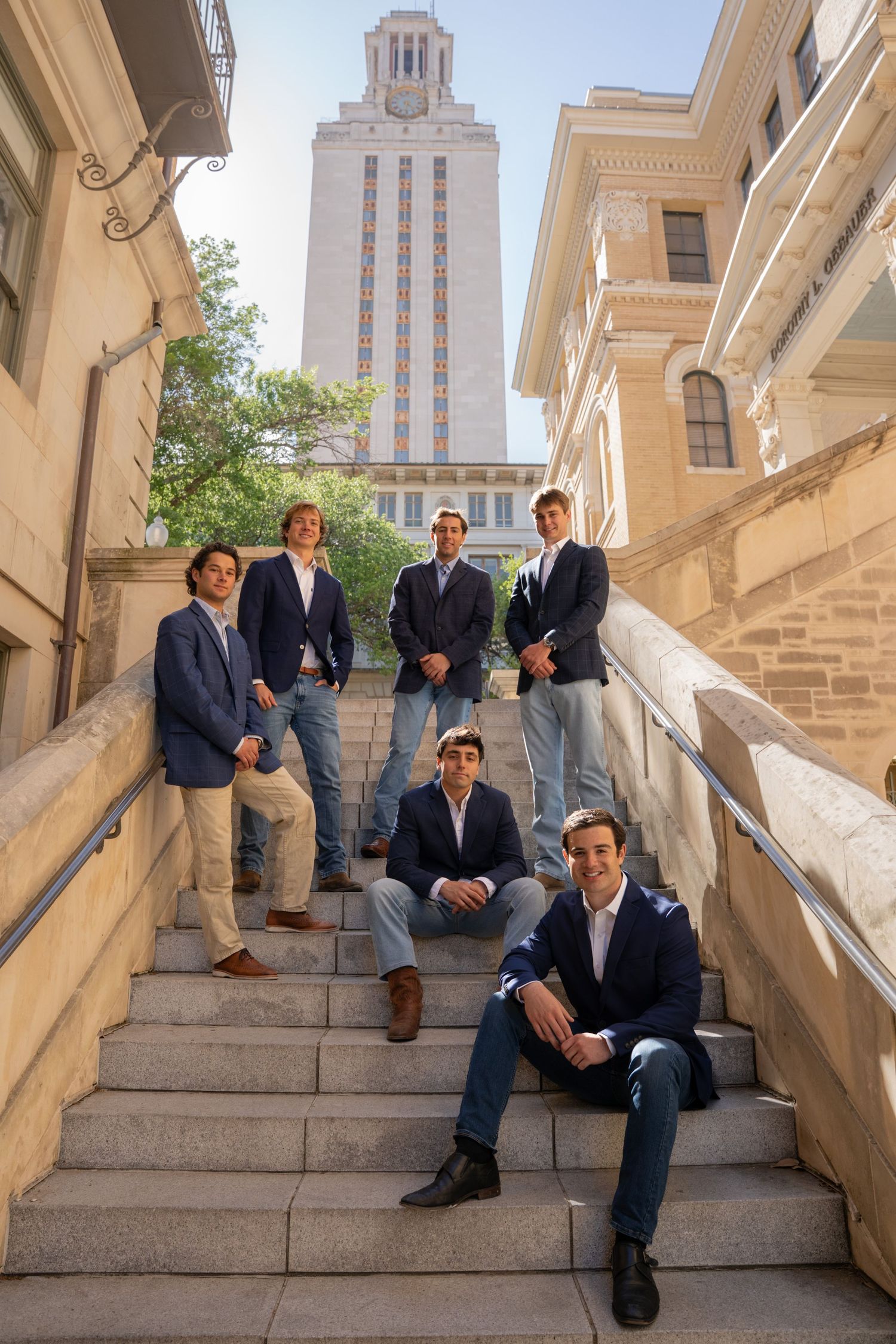 Group portrait of wedding attendees standing in a line against an ornate classical building exterior.
