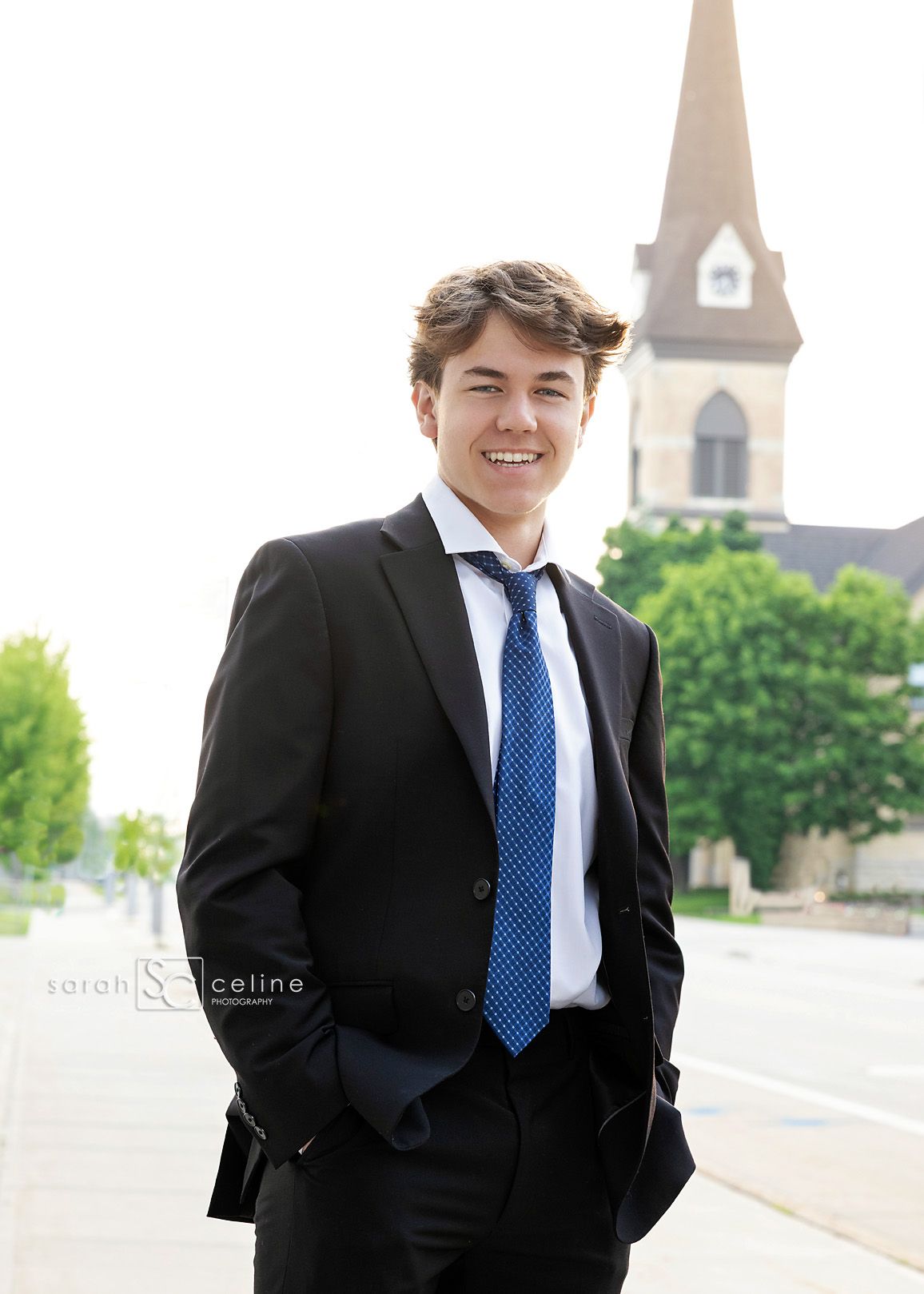 Young man in formal black suit and blue tie standing outdoors against church backdrop in four similar poses.