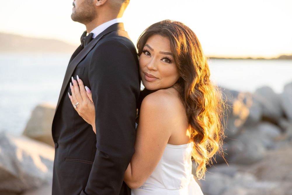 A couple embraces during a romantic sunset wedding photoshoot along a rocky coastal shoreline.