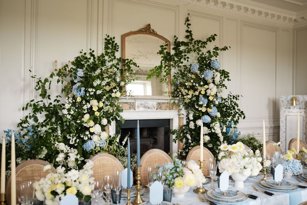 Long banquet table with white floral arrangements and greenery against paneled walls.