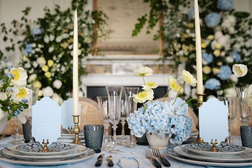 Elegant table setting with white flowers, blue accents, and gold candlesticks in a formal dining room.