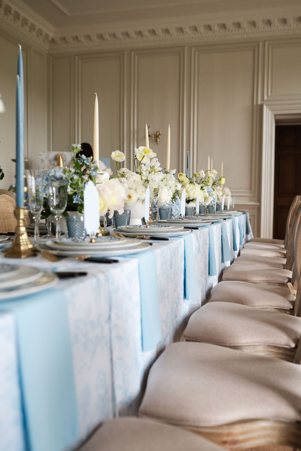 Luxurious dining setup with light blue tablecloths and cream-colored chairs in an elegant room.