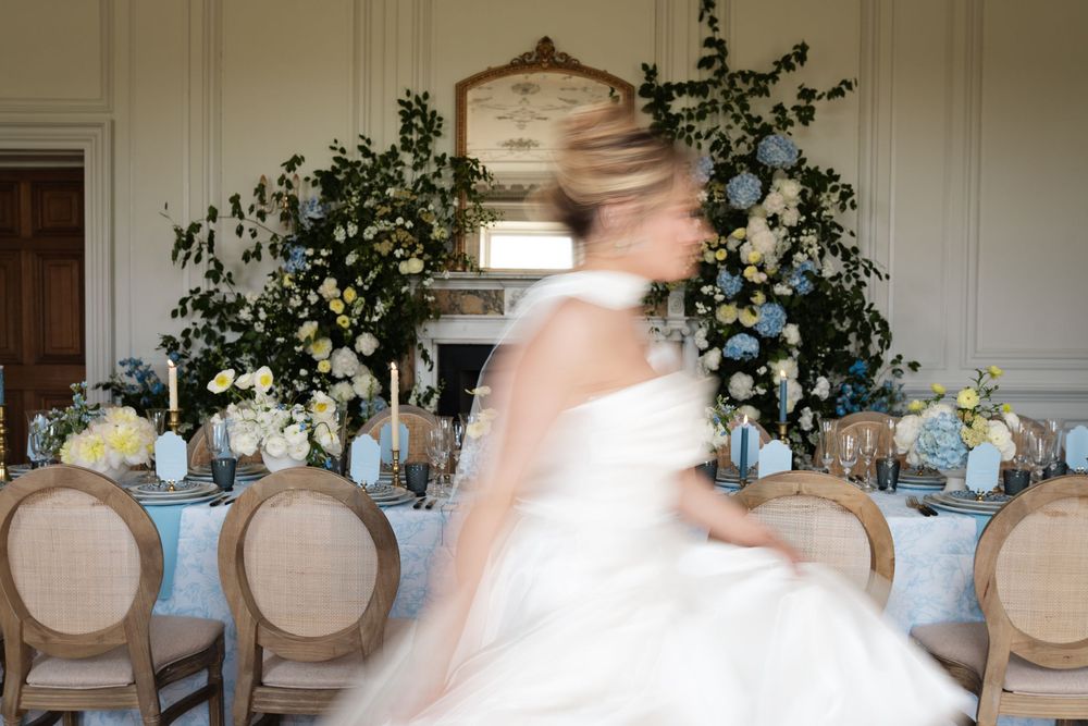 Romantic wedding reception decor with cream-colored chairs and blue and white floral arrangements.
