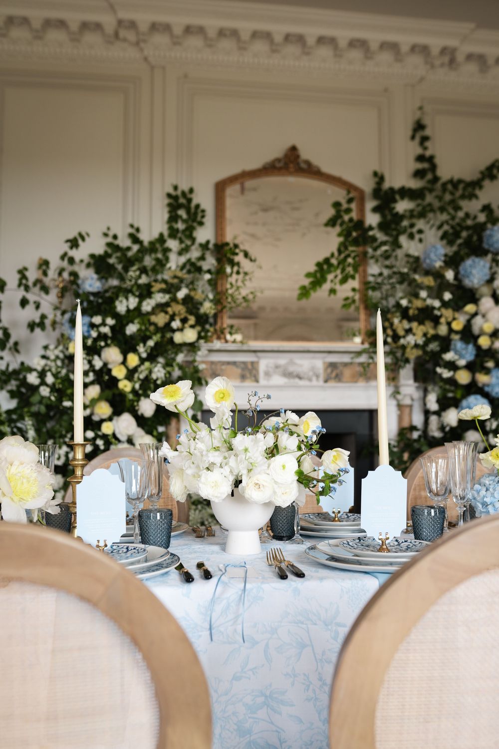 Luxurious table setting with white and blue florals around vintage mirror and fireplace.