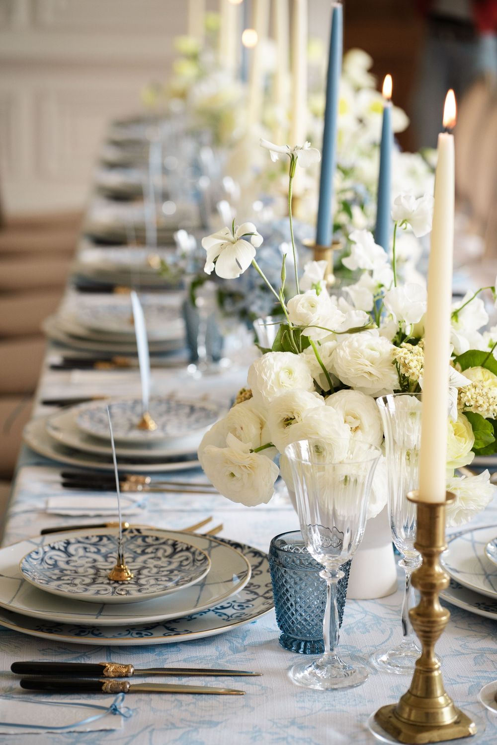 Close-up of formal place settings with blue and white plates, gold candlesticks, and white floral centerpieces.