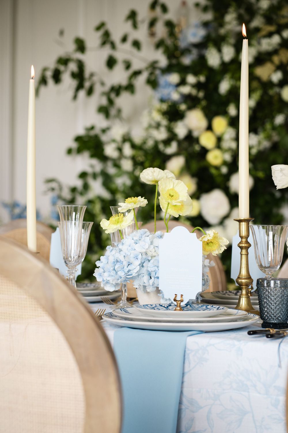 Table decorations featuring hydrangeas, white roses, and brass candlesticks with pale blue accents.