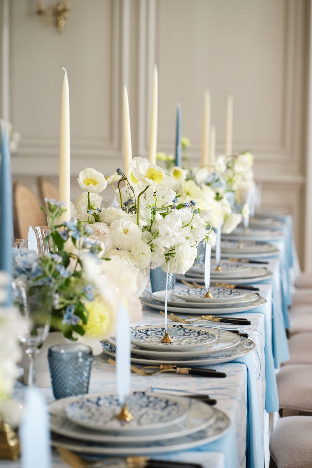 Elegant table setting with blue linens, white flowers and tall taper candles.