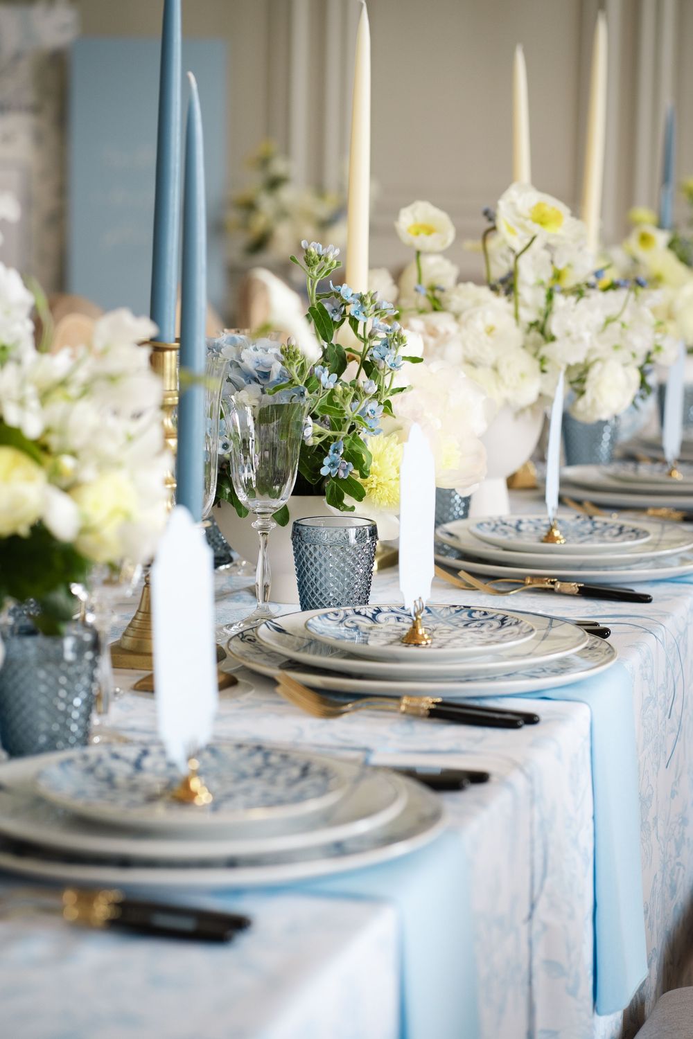 Elegant table setting with blue and white decor featuring tall tapered candles and fresh flowers.