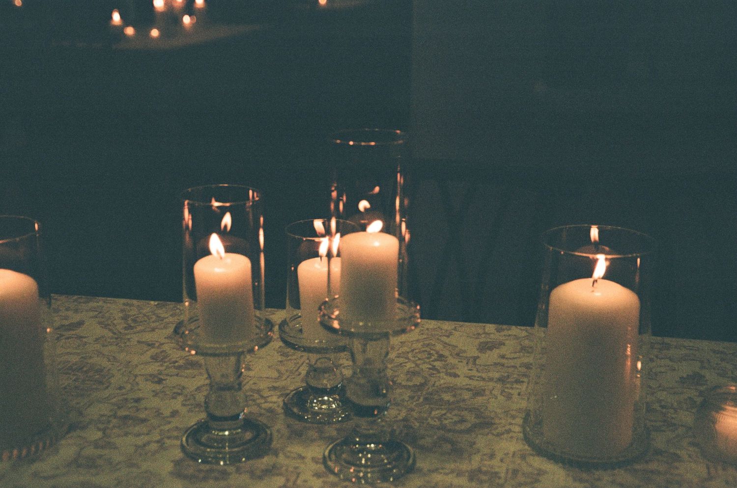 Glowing white pillar candles in glass holders create a romantic ambiance on a textured tablecloth.