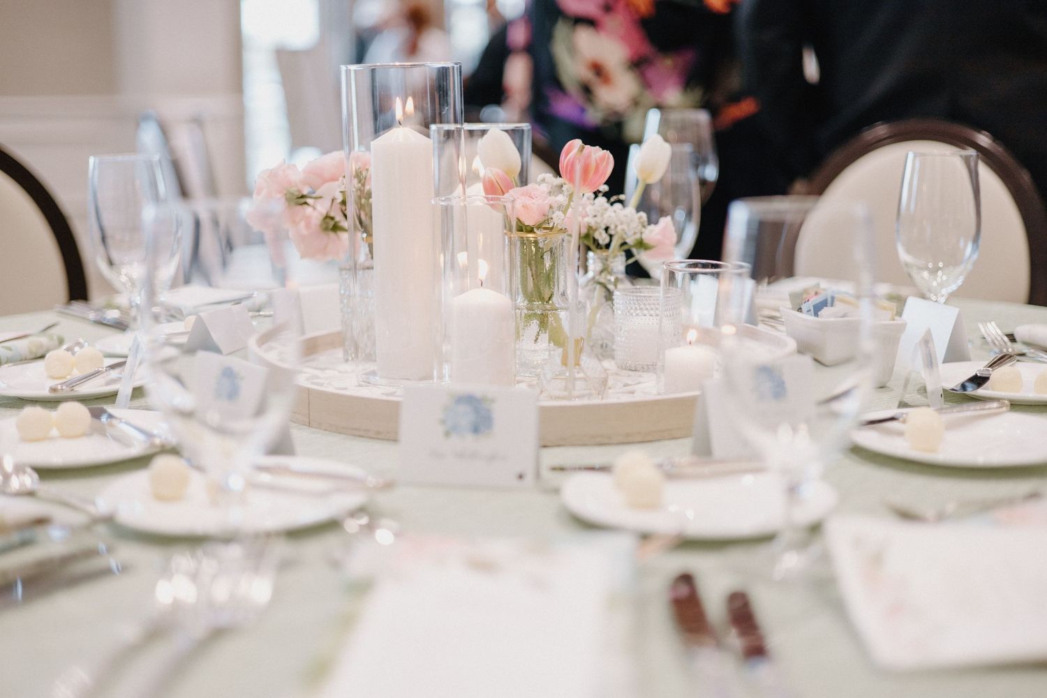 Elegant wedding reception table setting with pink roses, tall white candles, and crystal glassware on white tablecloth.