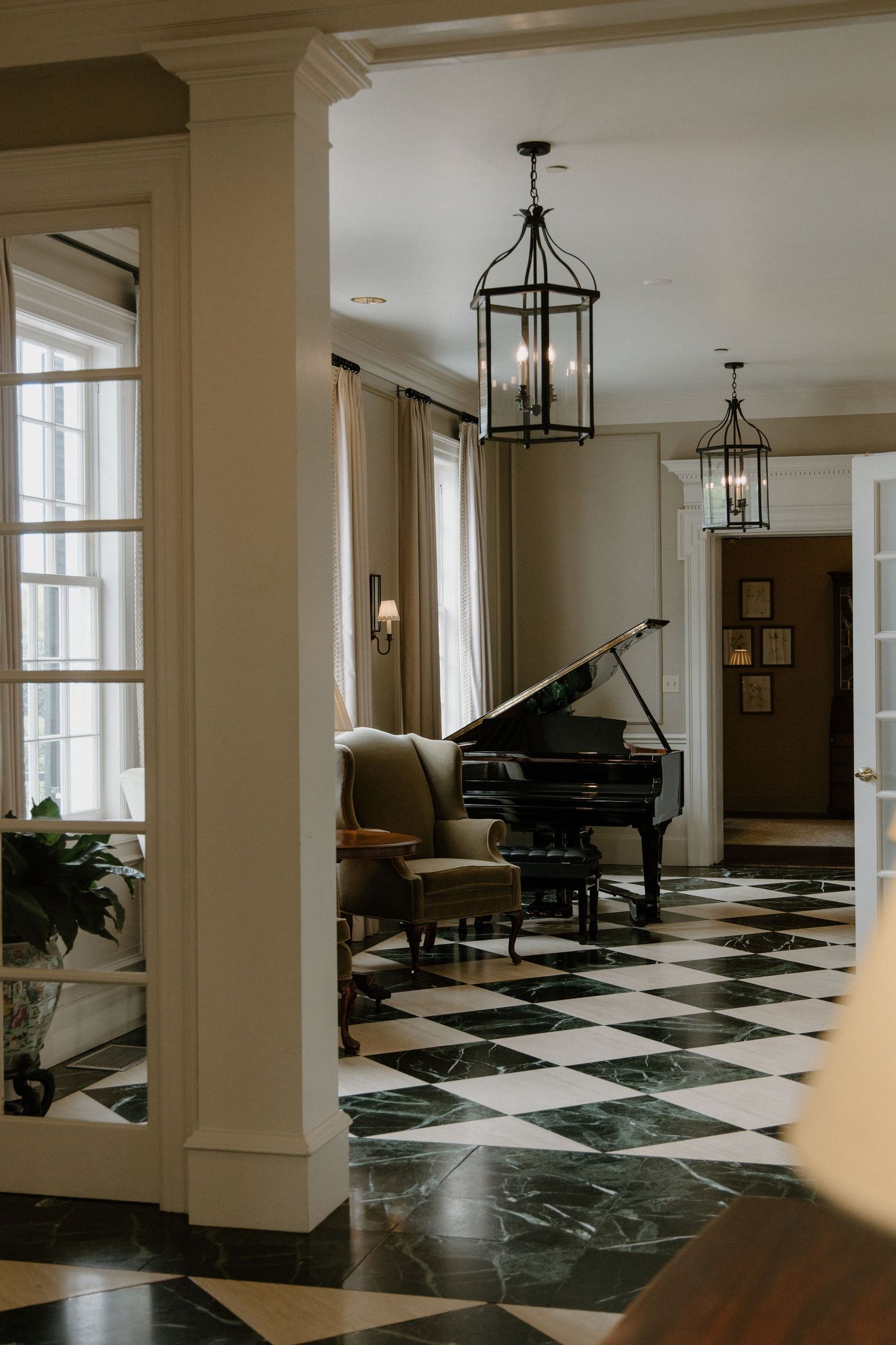 Elegant foyer with black and white checkered marble floors, lantern pendant lights, and a grand piano in warm natural light.