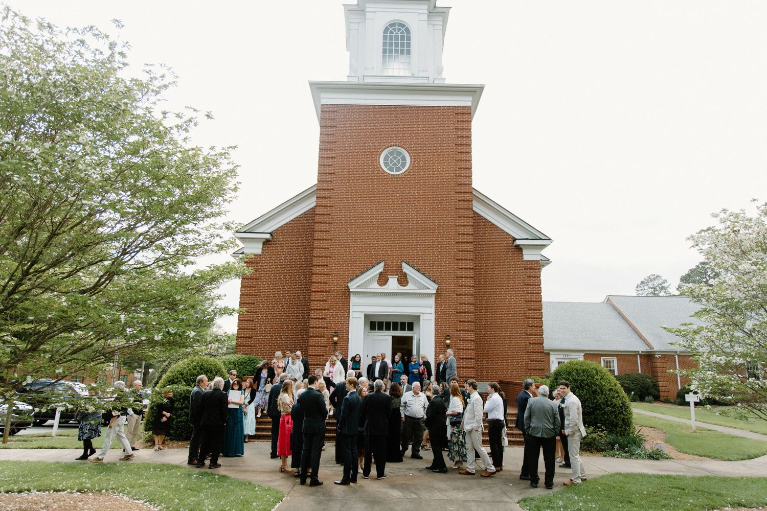 Wedding guests gather in front of a historic brick church after a ceremony.