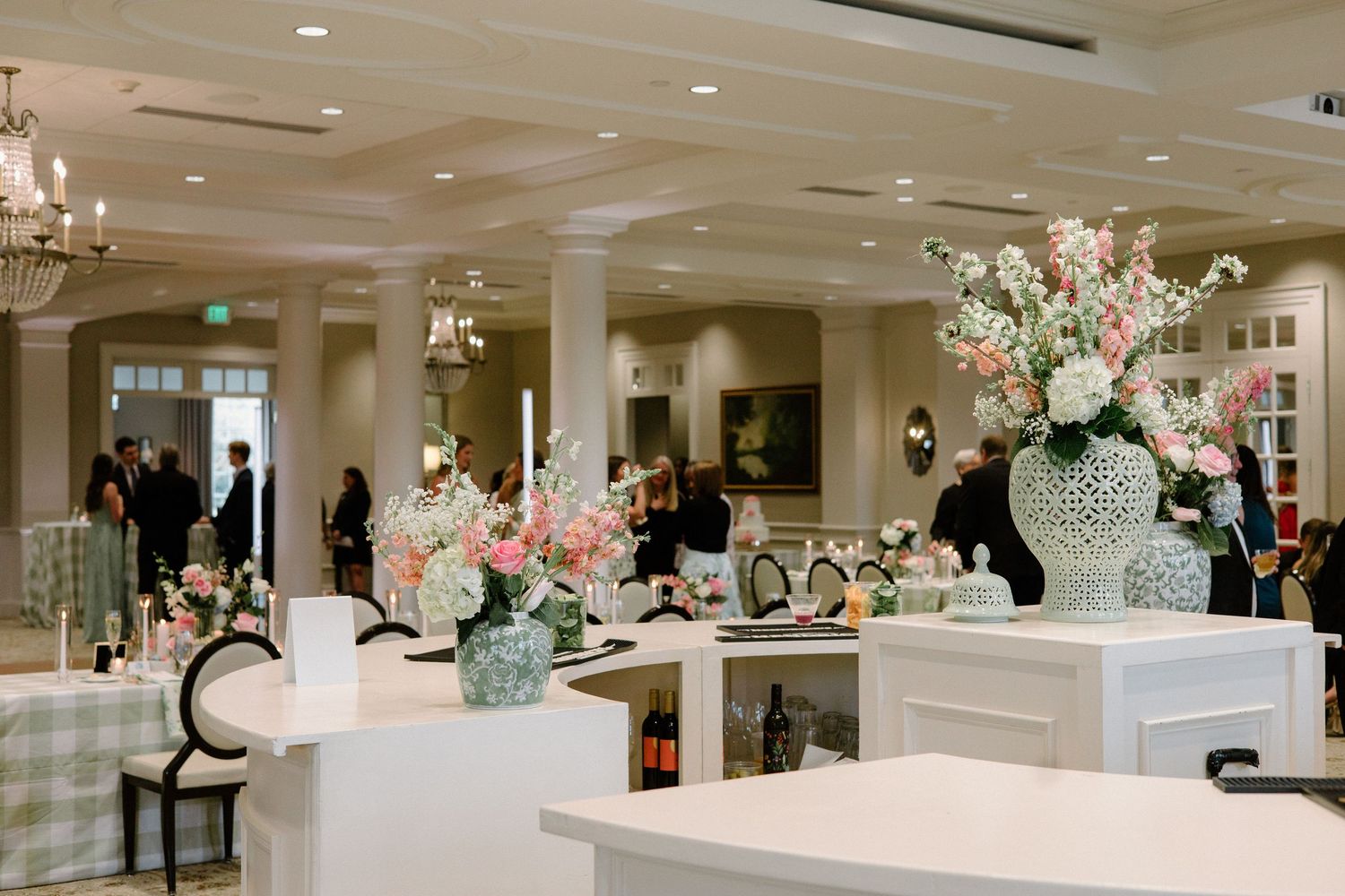 Elegant white ballroom with crystal chandeliers set up for a wedding reception featuring floral centerpieces and round tables.