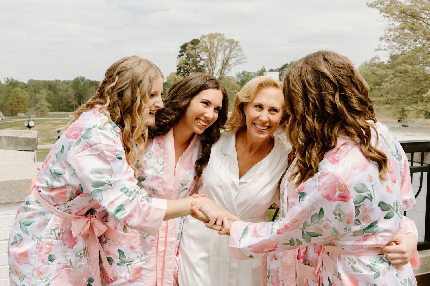 A group in matching floral robes share joyful laughter and hugs during a gathering outdoors.
