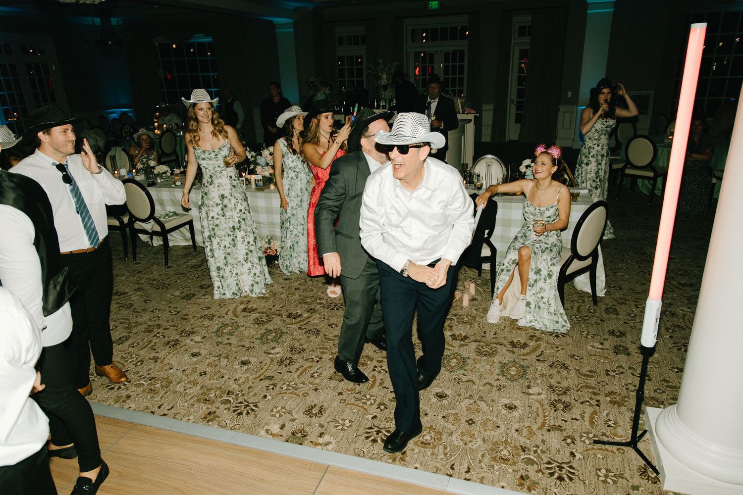 People dancing at a party with confetti on the floor, with white columns visible in the background.
