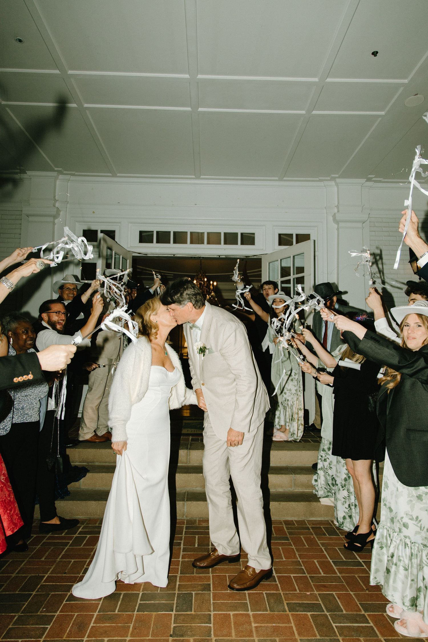 Newlyweds share a romantic moment during reception send-off as guests create a sparkler tunnel in an elegant venue.