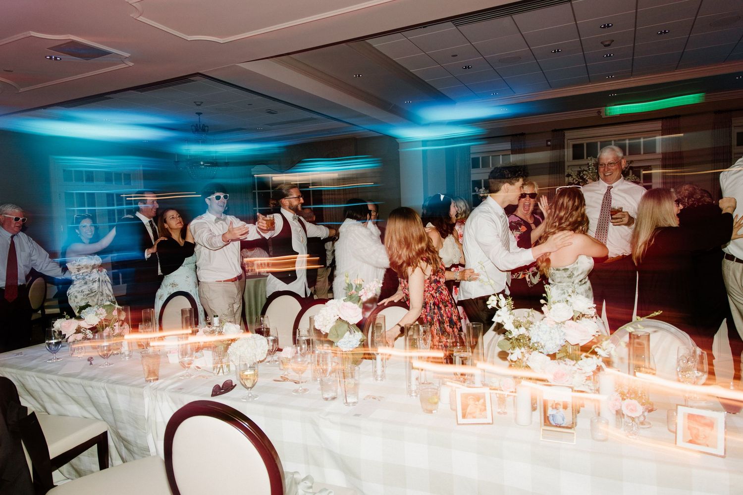 Reception tables at a wedding venue with decorative lighting and party guests mingling in a teal-lit room.