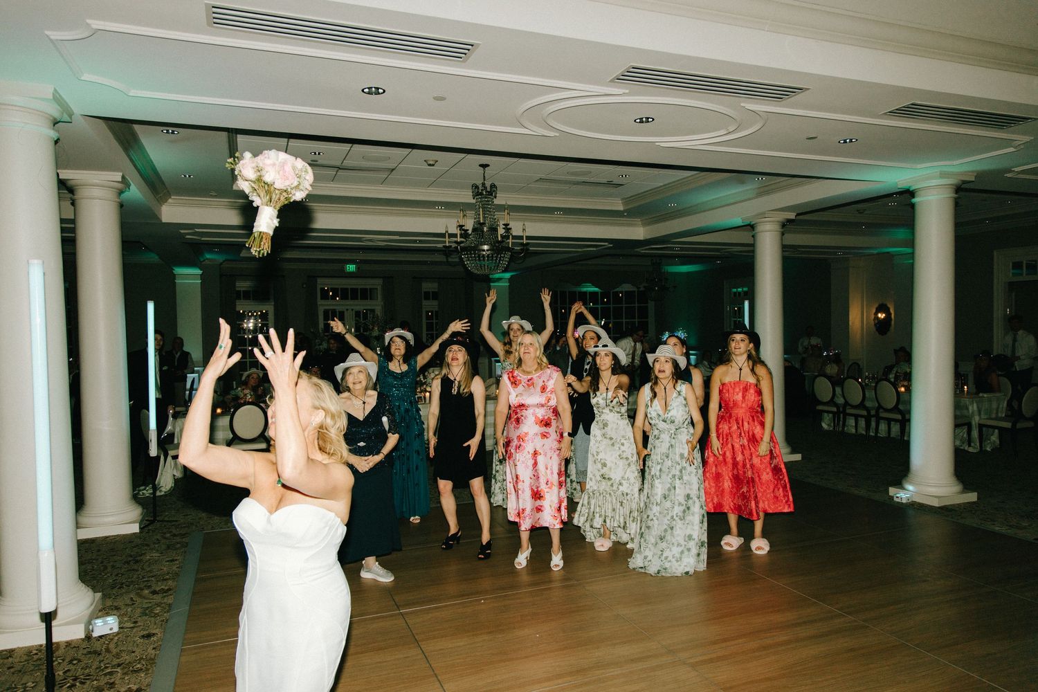 A group of partygoers on a dance floor throwing their hands up in celebration during a wedding reception.