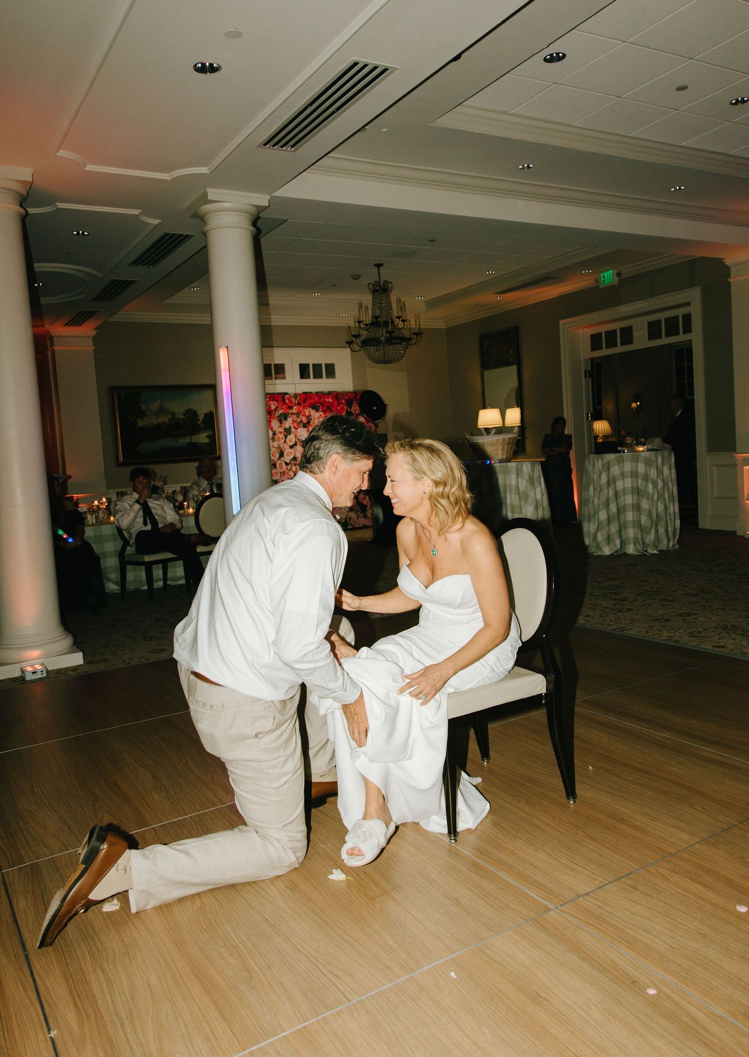 A couple sharing a romantic moment on the dance floor at a wedding reception with columns and chandelier visible.