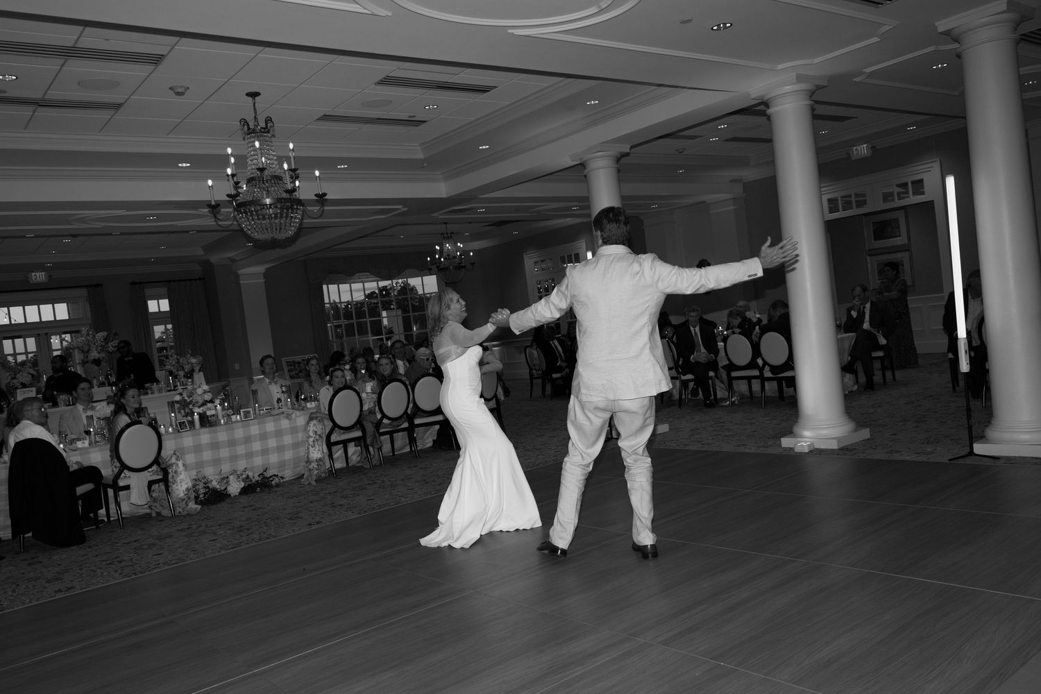 A couple performs a dramatic dance move in a black and white photo on an elegant ballroom dance floor.