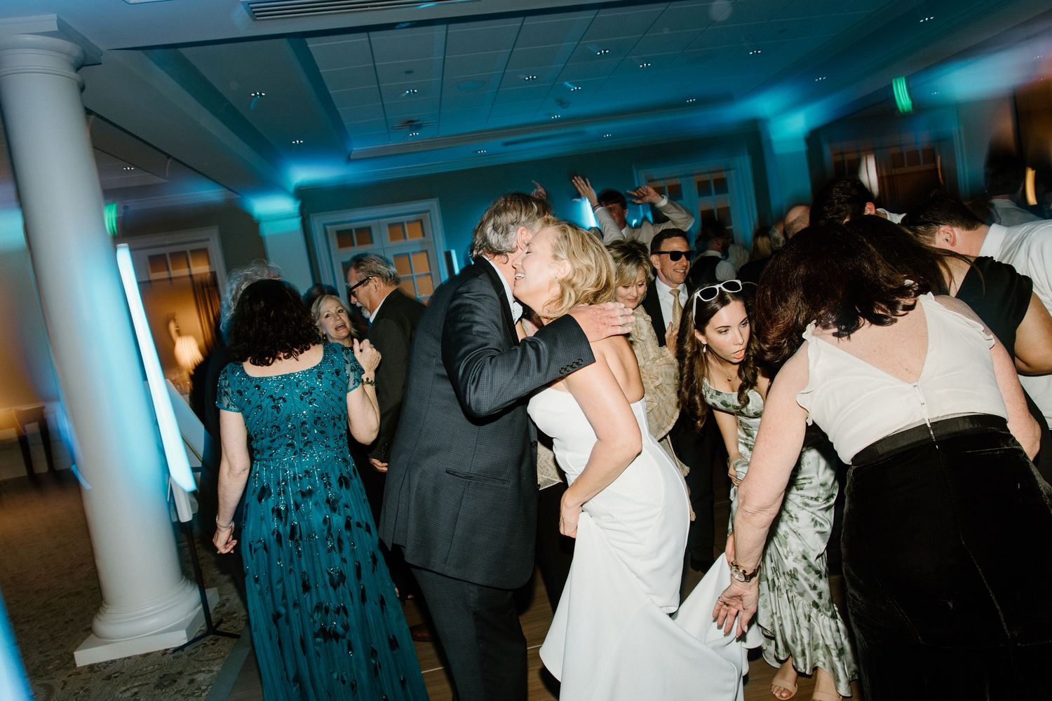 People dancing together at a wedding reception under blue atmospheric lighting in an elegant venue.