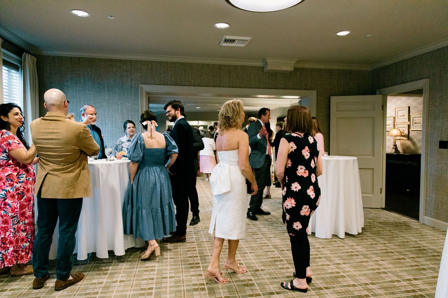 People gather and mingle around cocktail tables at an indoor event reception with teal walls.