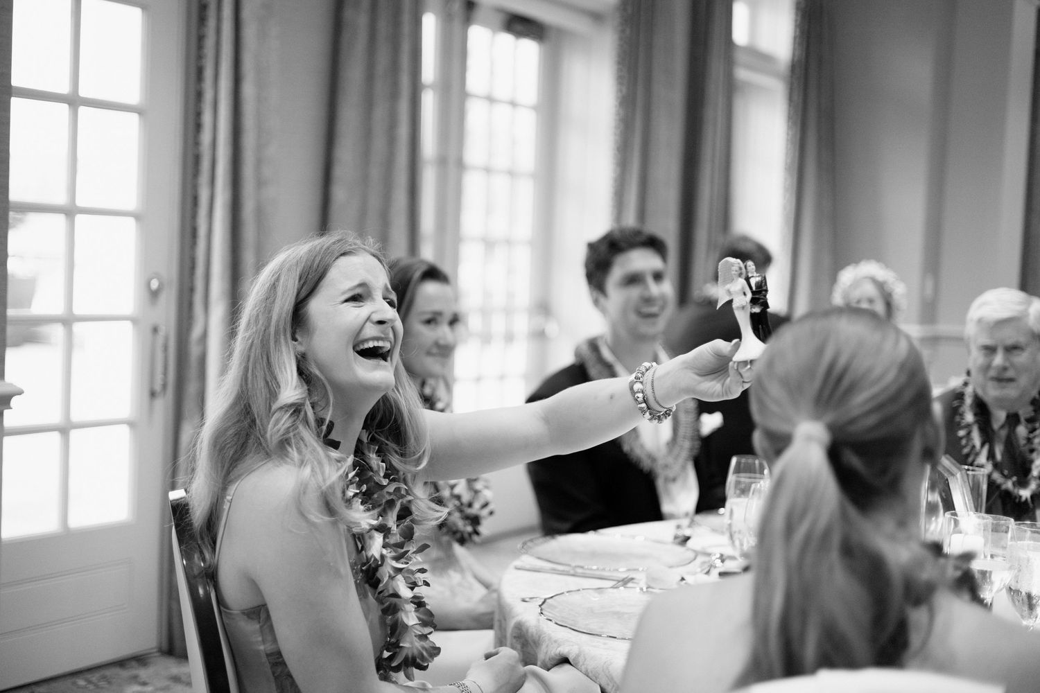 Guests laughing and interacting with joy during a celebratory moment at an elegant indoor dinner reception.