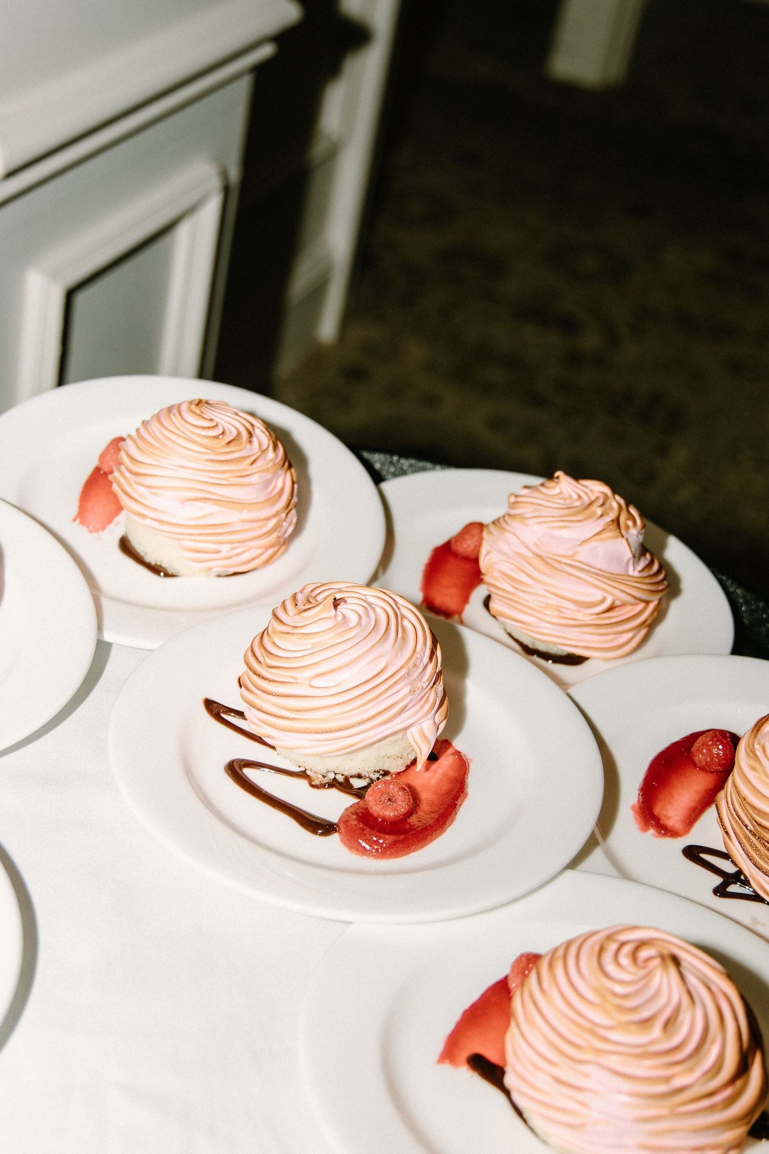 Pink meringue desserts with fresh strawberries and chocolate drizzle arranged on white plates.
