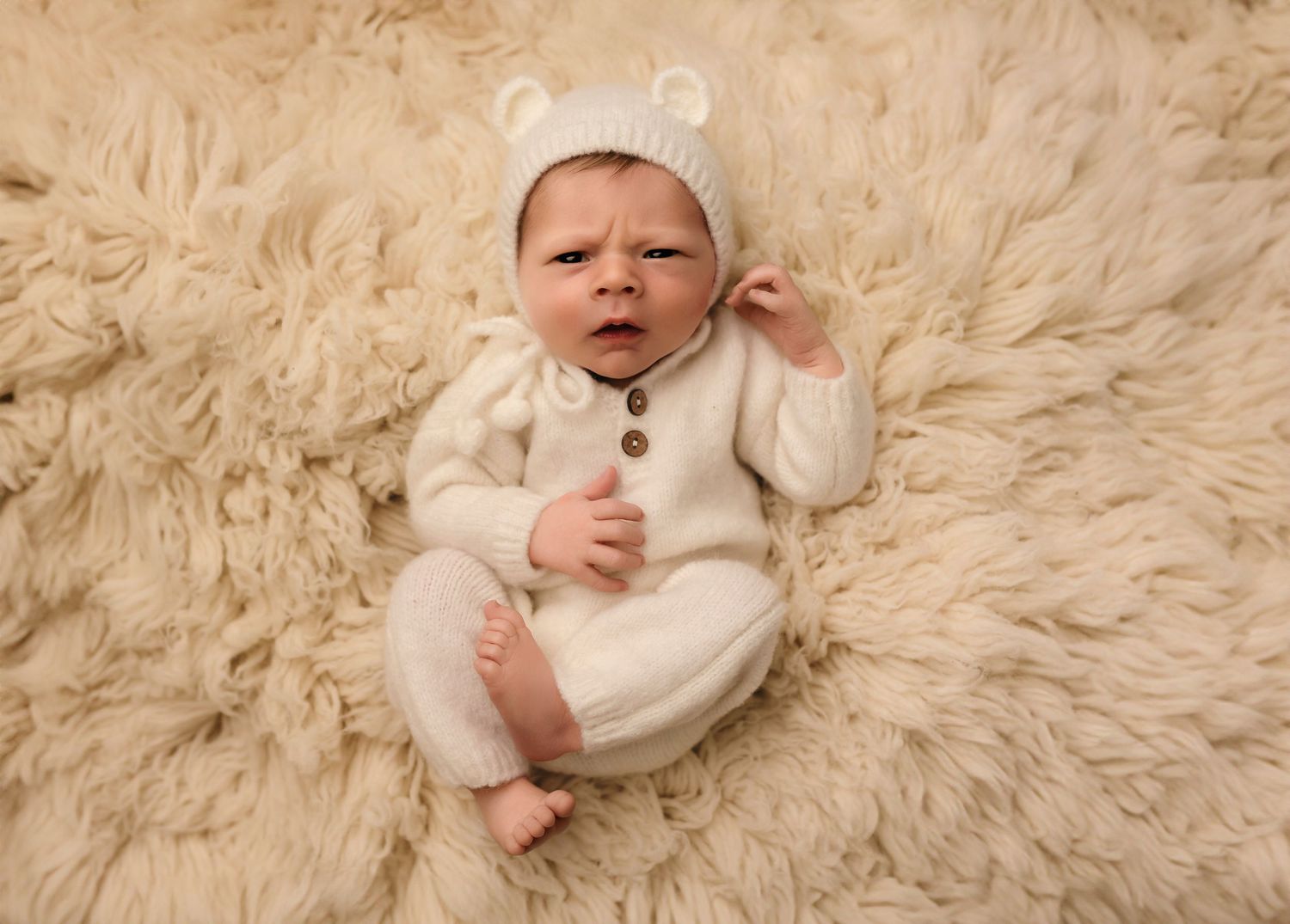 Charlottesville photographer, newborn, maternity, and family, baby dressed in white knits with bear ears and lying against a cream rug.