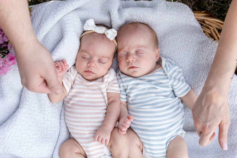 Two sleeping newborn twins in striped onesies lying on a soft blanket outdoors.
