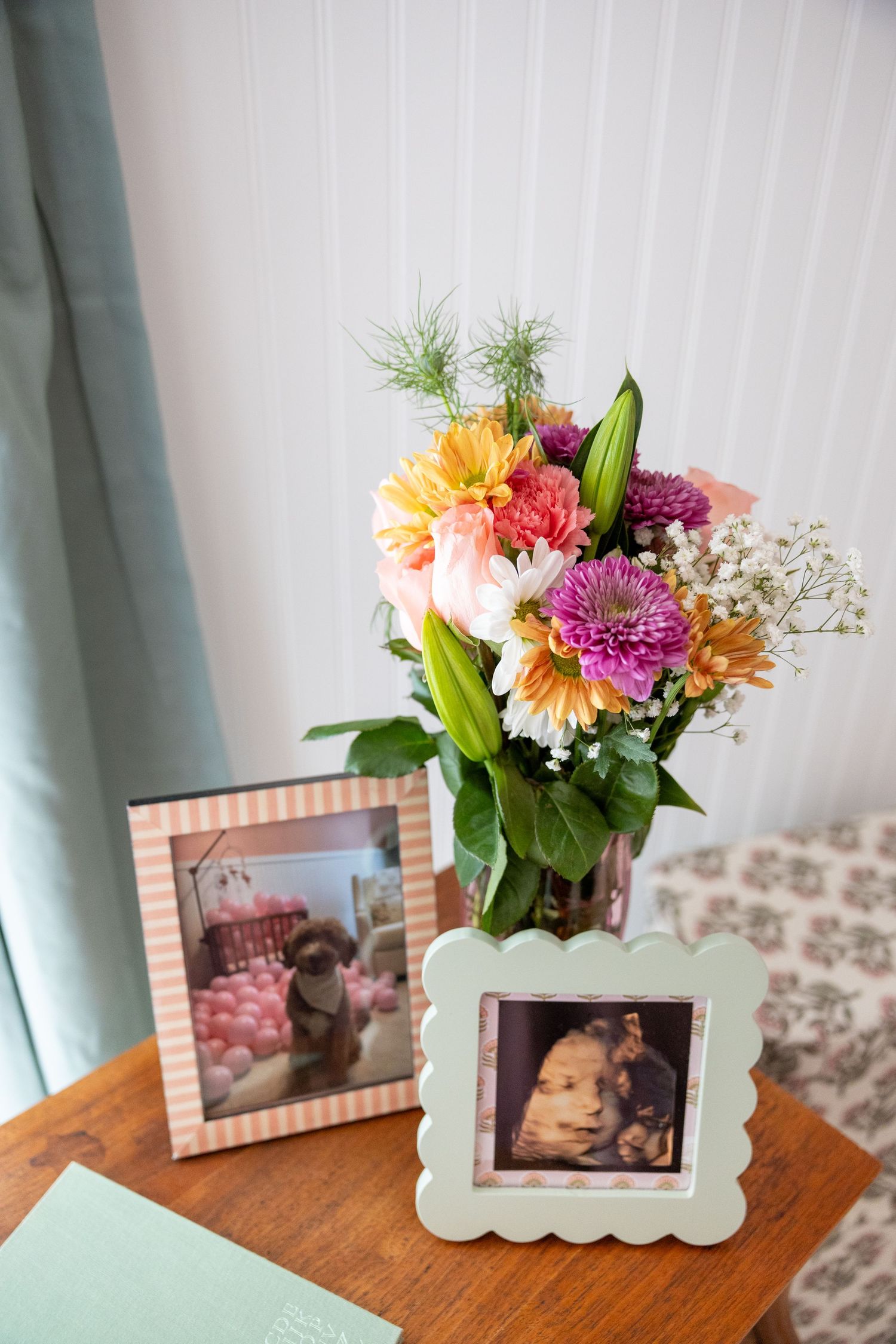 A vibrant floral arrangement with dahlias and baby's breath sits next to framed photos on a wooden surface.Raleigh Newborn Photography