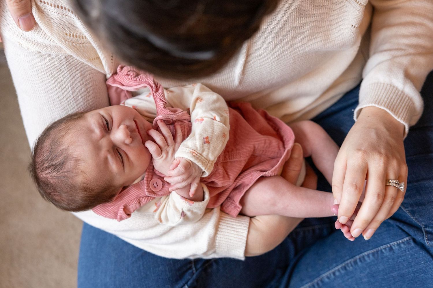 A newborn baby wearing pink clothing sleeps while being held in someone's lap.