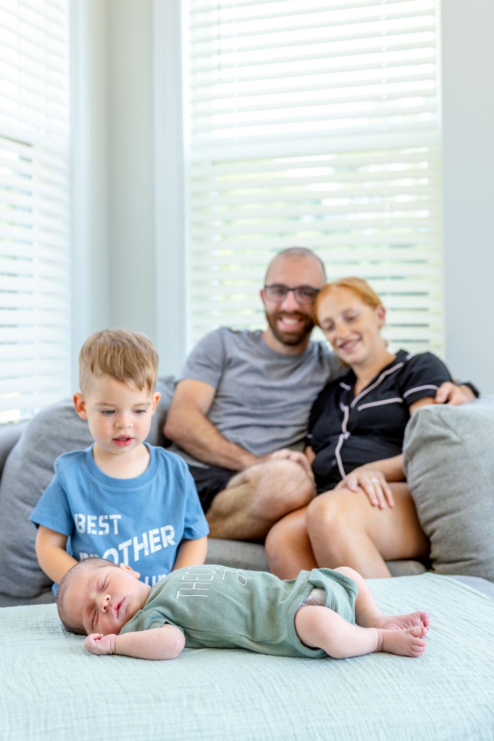 Family portrait with parents on sofa, brother watching over sleeping newborn baby in their Smithfield, NC at home newborn session.