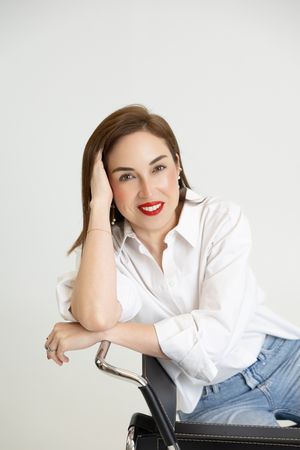 Professional portrait of someone in a crisp white button-down shirt and jeans posing casually against white background.