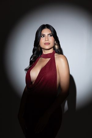 Dramatic studio portrait with dark shadows and burgundy halter dress against black and white gradient background.