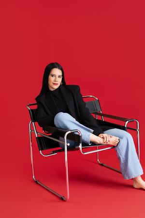 Stylish outfit featuring black turtleneck and blazer paired with light denim on red backdrop.