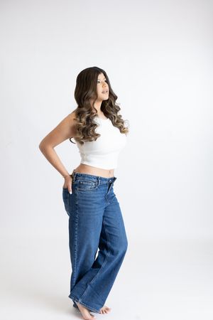 Woman in white crop top and loose blue jeans poses against light background in studio setting.