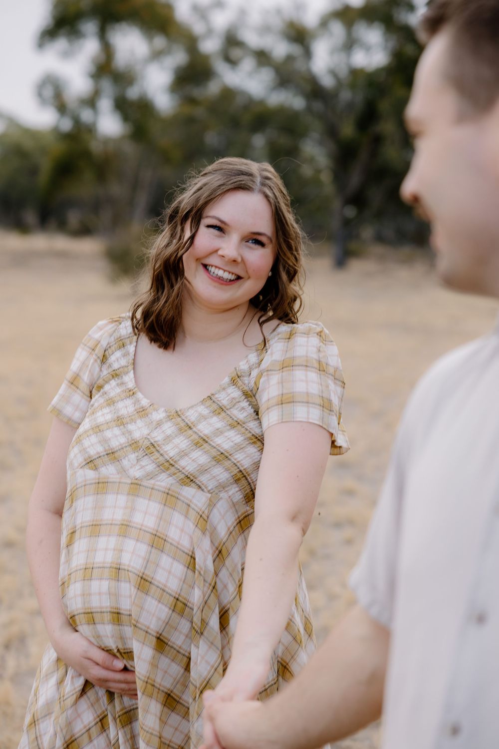 A person wearing a yellow plaid dress poses and smiles outdoors in golden sunlight.