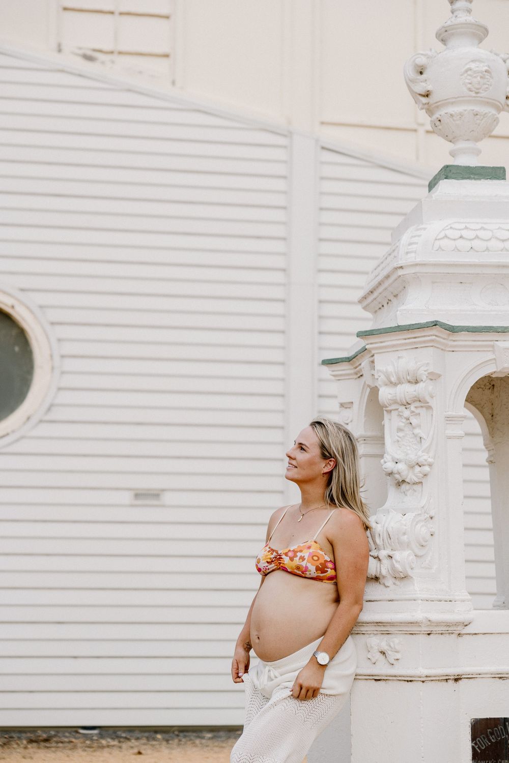 A maternity photo against a white church facade with ornate architectural details.